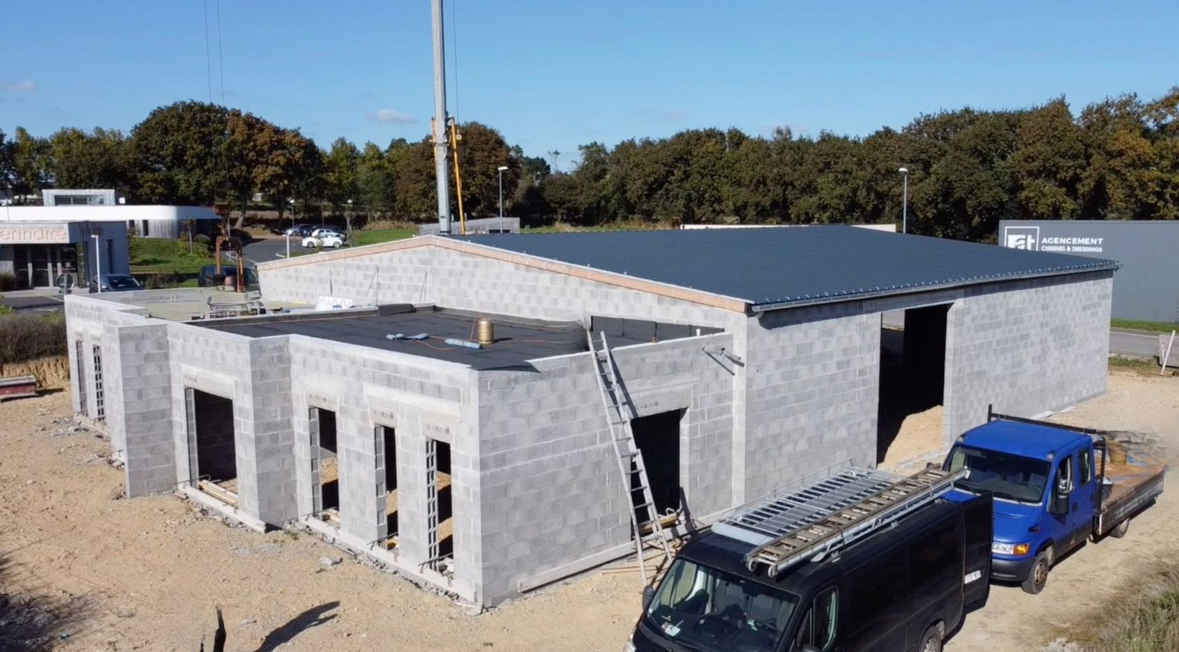Maison moderne de deux étages en construction, avec échafaudages et toiture inachevée, sur un terrain en terre battue.