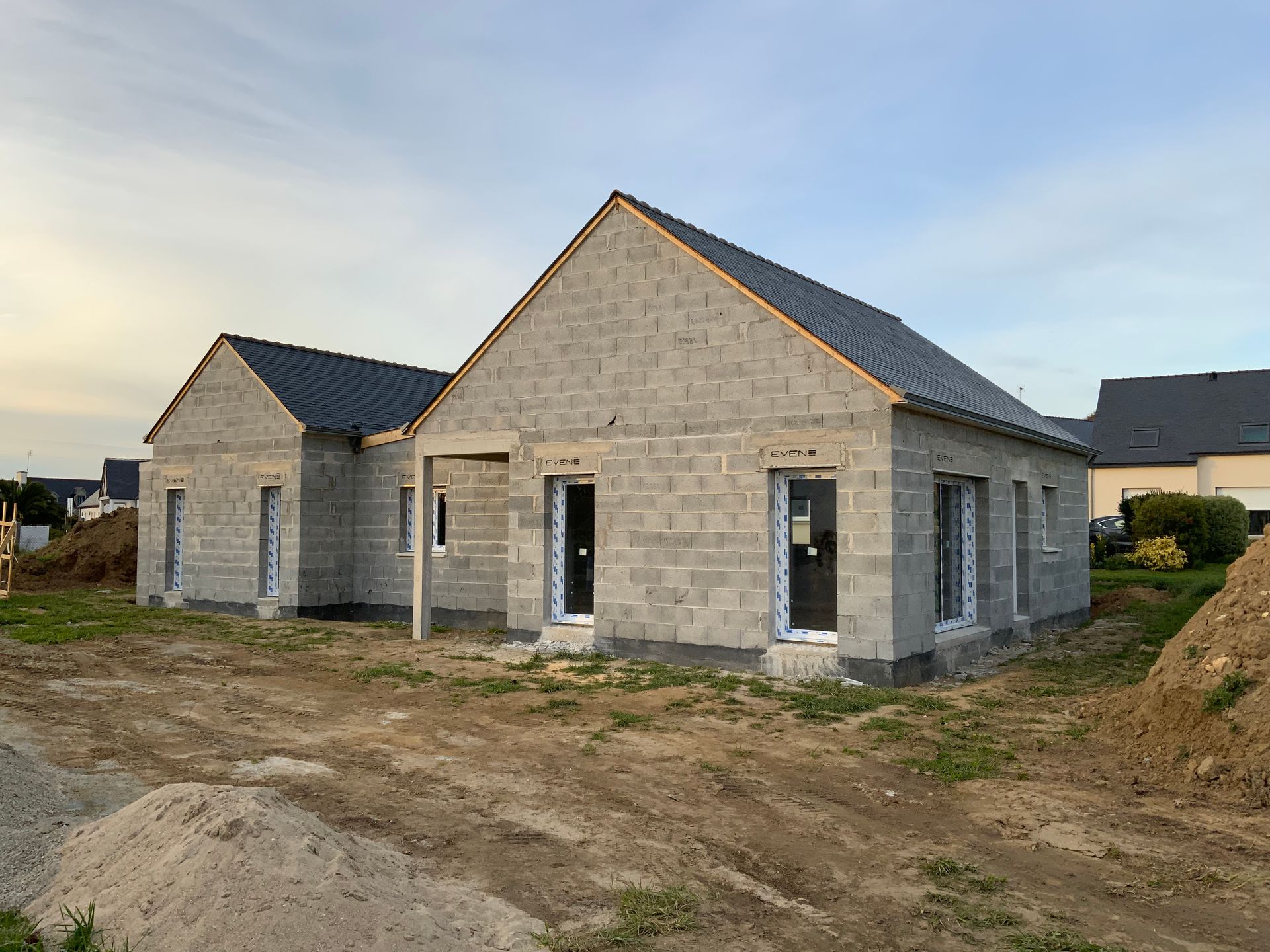 Maison en parpaings en construction, charpente de toit en bois et ciel bleu.