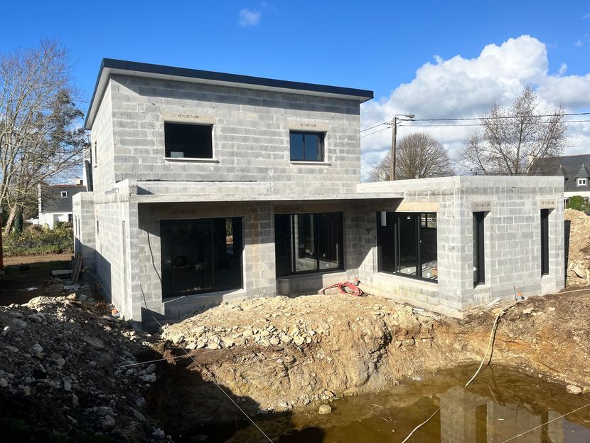Maison en briques partiellement construite, avec des parpaings empilés et une dalle de béton.