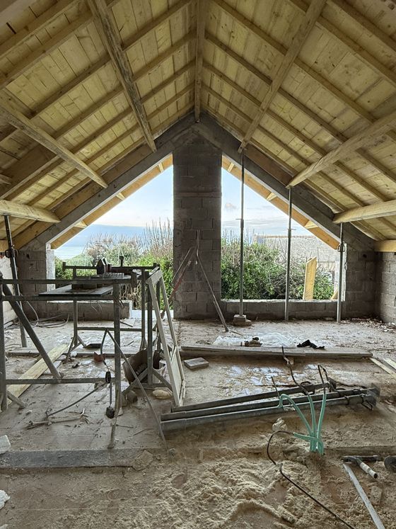 Pavillon extérieur partiellement construit, avec poutres de toit en bois apparentes et matériaux de construction à l'intérieur.
