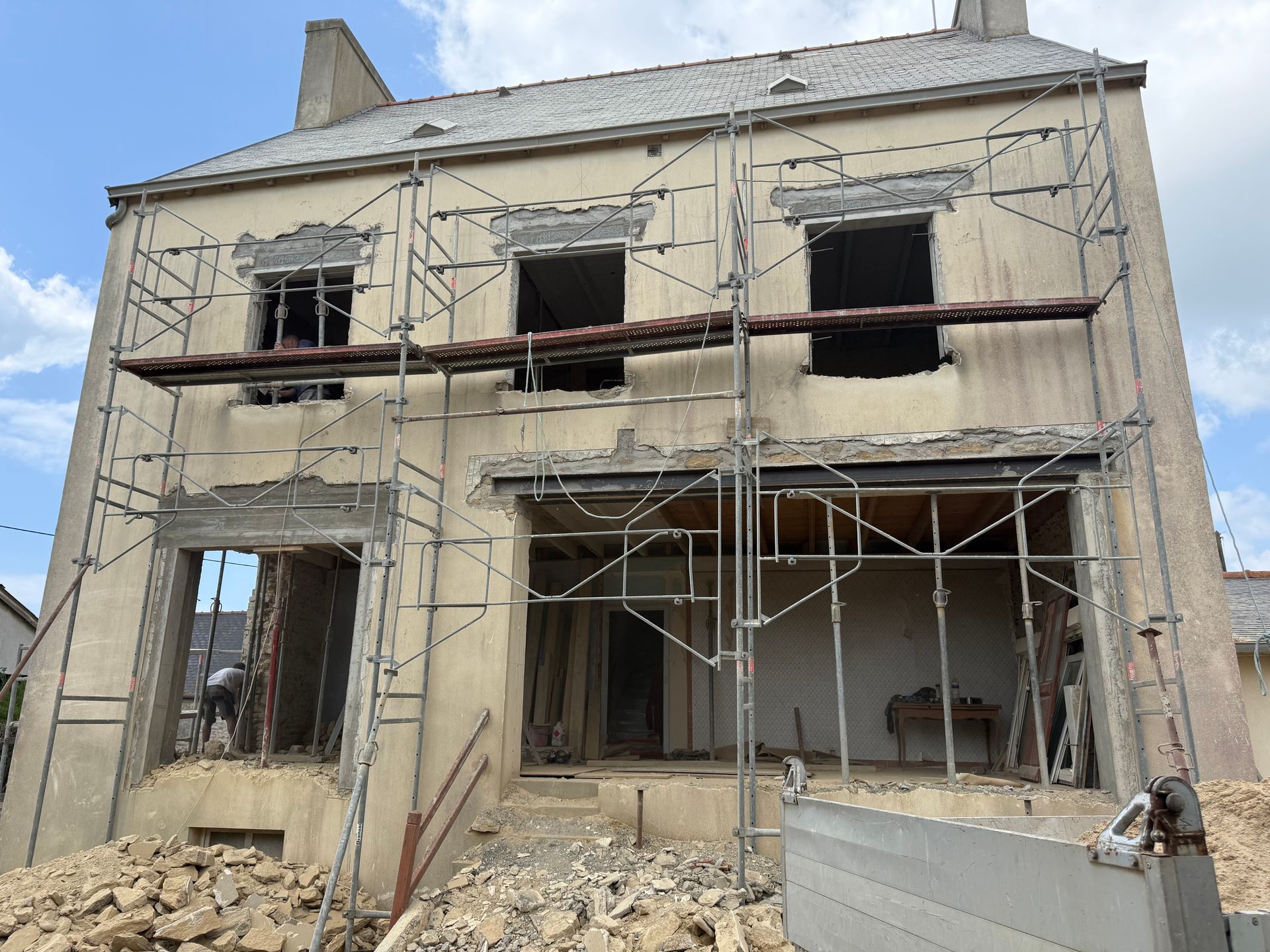 Intérieur d'un chantier de construction avec murs en parpaings blancs, poutres en bois apparentes et charpente de plafond.
