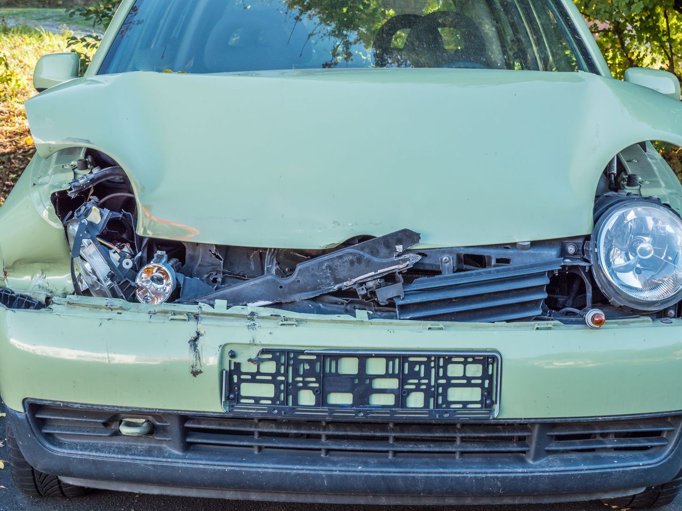 Vue de face d'une voiture vert menthe avec l'avant fortement endommagé et les phares cassés.