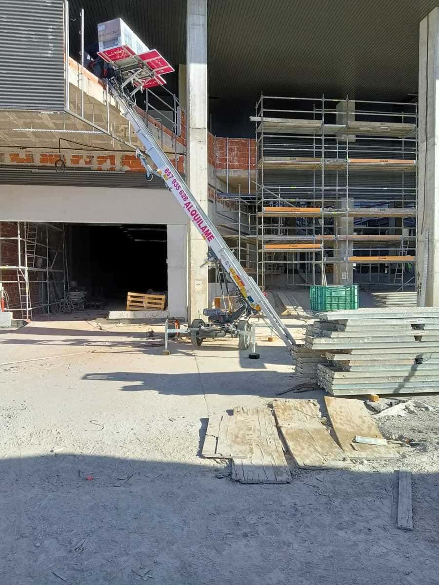 Obra: un ascensor sube una caja hacia un edificio. Se ven andamios y escombros.