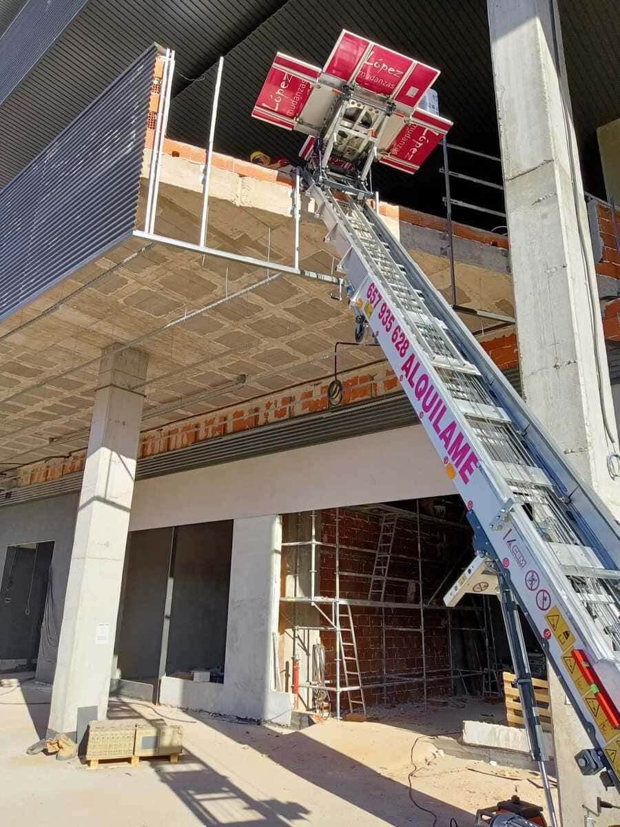 Un sitio de construcción con un elevador de material rojo y plateado que transporta artículos a la abertura de un edificio.