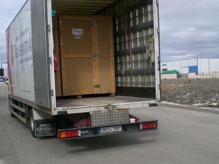 Camión abierto, cajas de carga cargadas, estacionado sobre asfalto, entorno industrial.