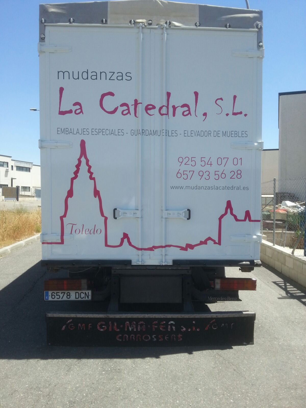 Camión de mudanzas blanco con texto rosa y una silueta de Toledo, España.