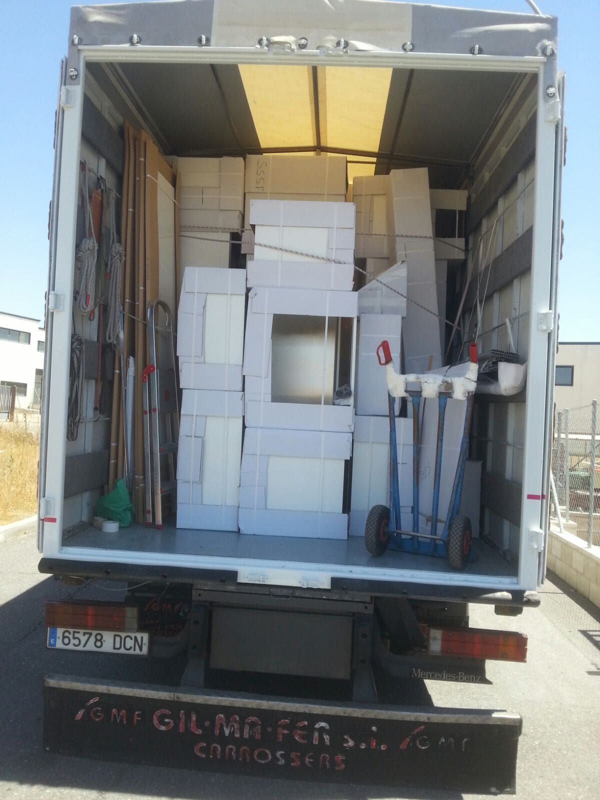 Parte trasera de un camión cargado con varios artículos blancos empaquetados, posiblemente para una mudanza o entrega.