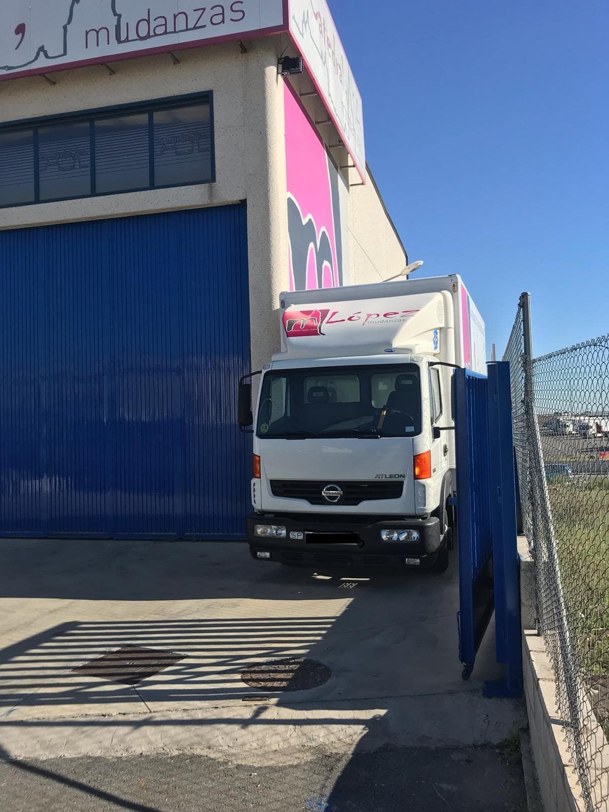 Camión de mudanzas blanco estacionado frente a un edificio con puerta azul y cartel rosa.
