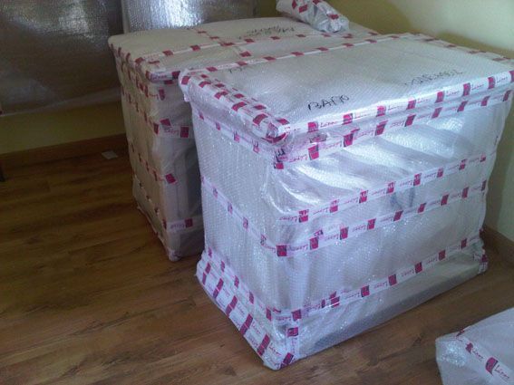 Dos cajas grandes envueltas con cinta roja, sobre un suelo de madera.