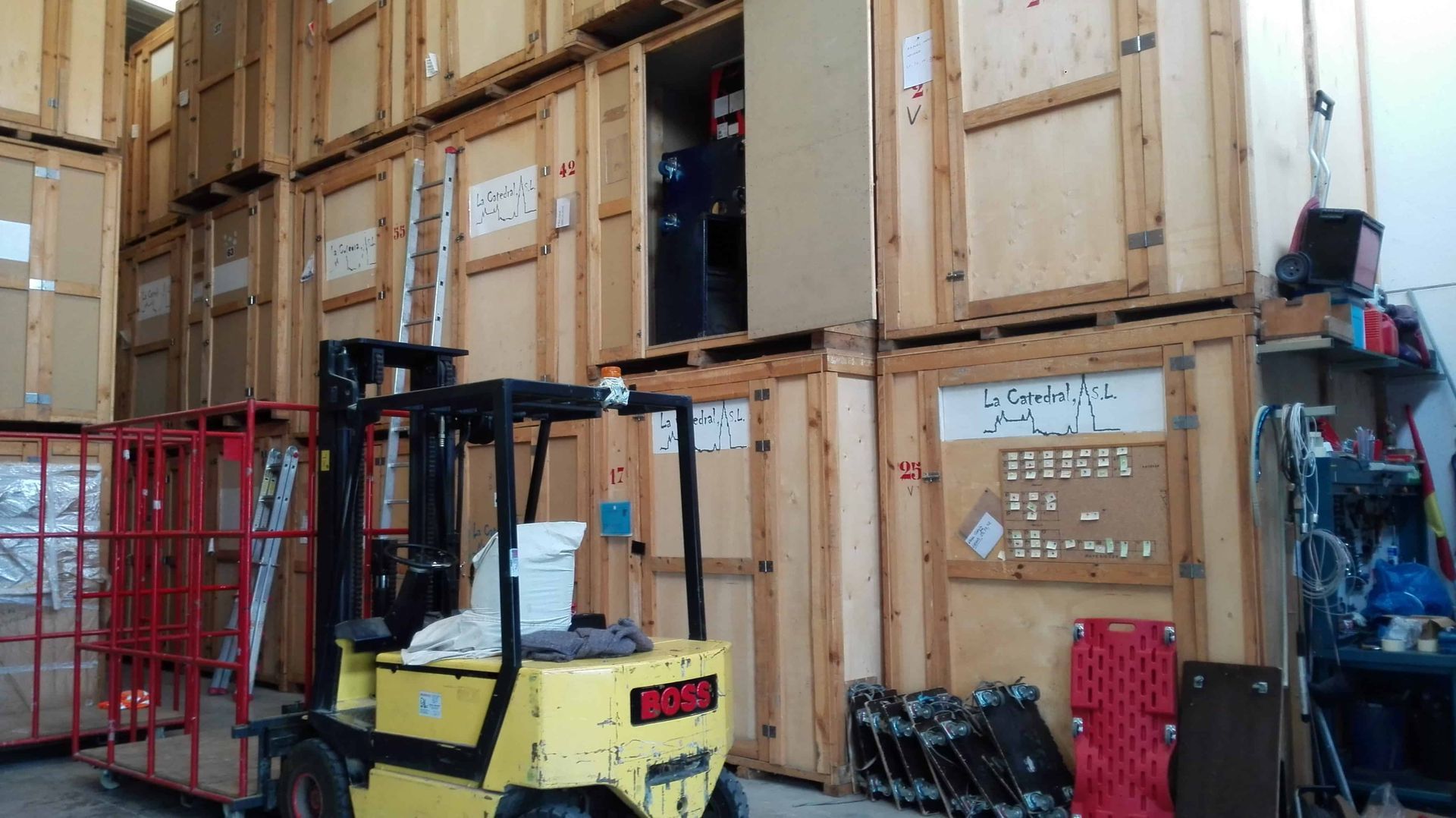 Carretilla elevadora amarilla en un almacén. Cajas de madera apiladas; una persona en la puerta de una caja abierta.