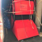 Equipo rojo atado dentro de un vehículo, probablemente para transporte. Ruedas visibles, lo que sugiere portabilidad.