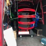 Dentro de una camioneta roja, una gran máquina circular, de color rojo y negro, descansa sobre una plataforma con ruedas.