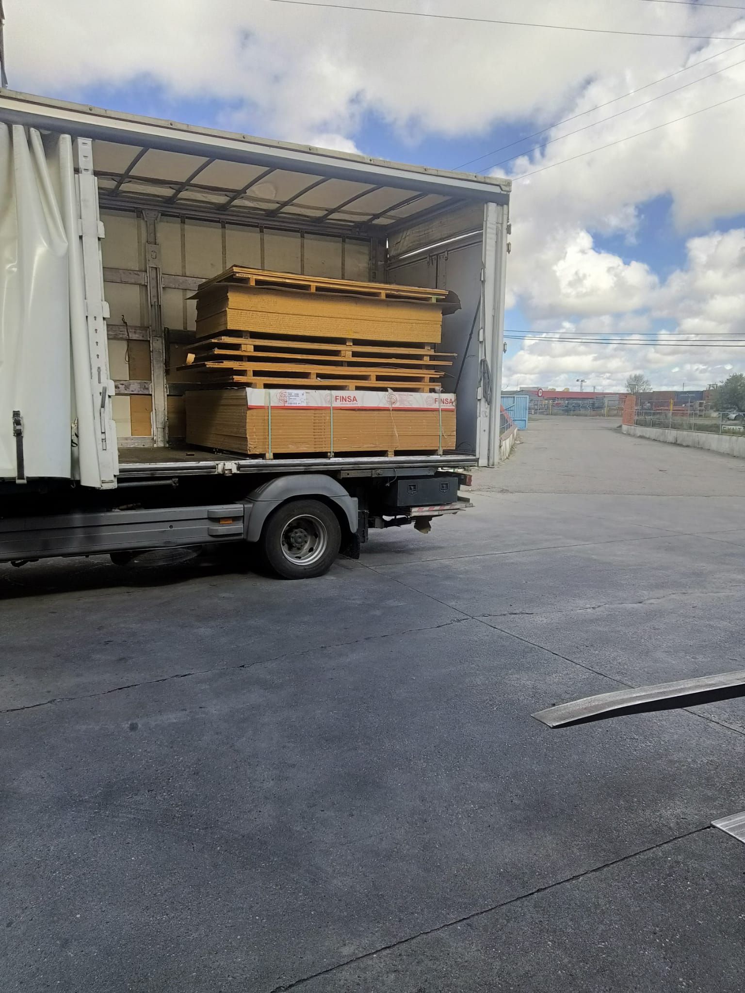 Un camión cargado con paletas de madera en un terreno pavimentado bajo un cielo parcialmente nublado.