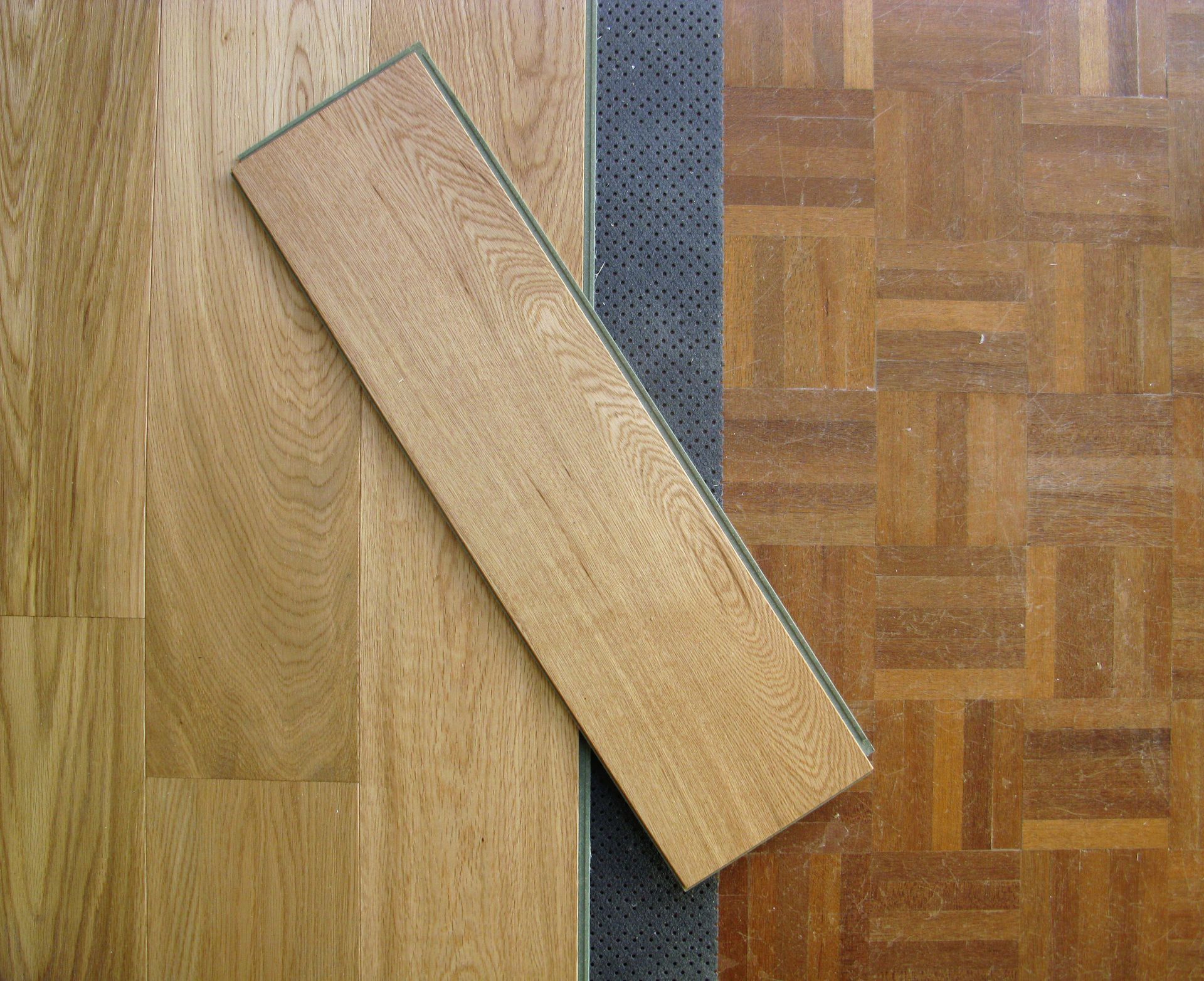 Échantillons de revêtements de sol en bois : lames, parquet et sous-couche noire côte à côte.
