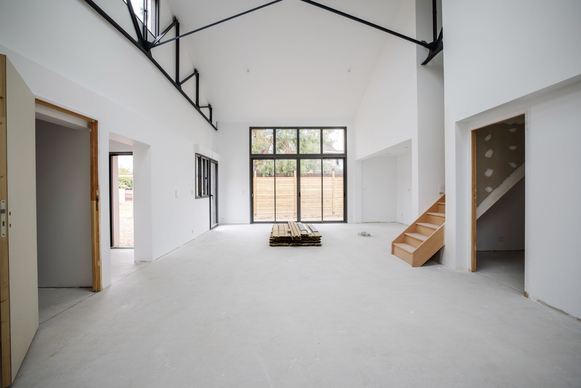 Intérieur spacieux aux murs blancs, avec de grandes fenêtres, des poutres apparentes et un escalier en bois.