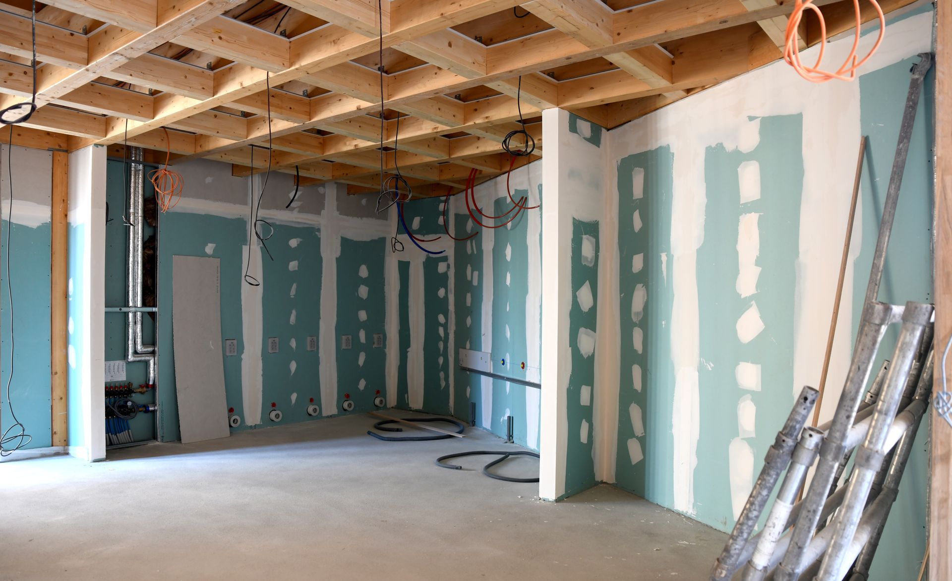 Intérieur d'une pièce en construction ; plafond en bois apparent, cloisons sèches, câblage et montants métalliques.