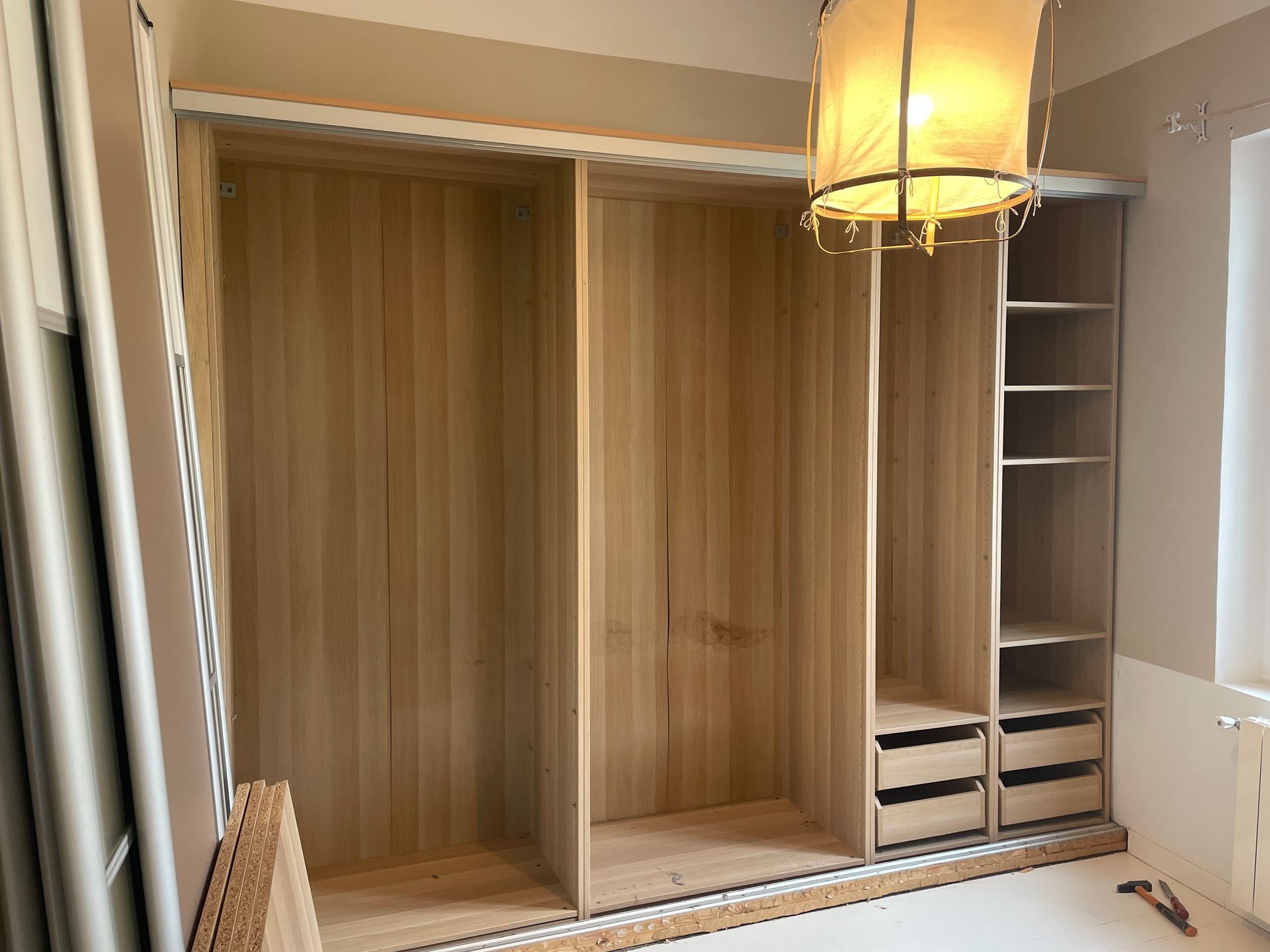 Placard intégré inachevé avec structure métallique, cloisons sèches, étagères ouvertes et tringle à vêtements.