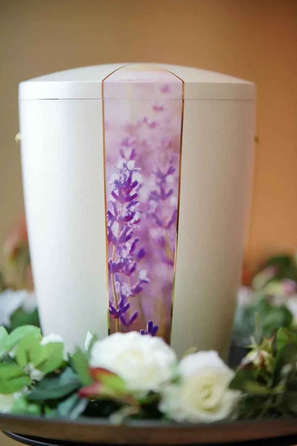 Eine weiße Urne mit violetten Blumen steht auf einem von Blumen umgebenen Tisch.