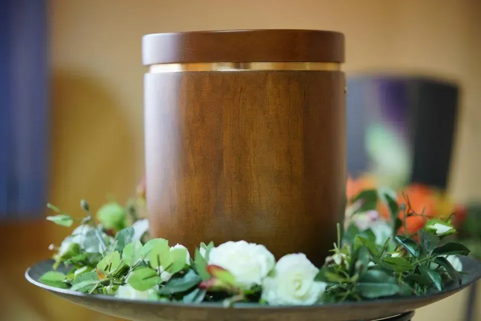 Eine hölzerne Urne, umgeben von Blumen auf einem Teller.