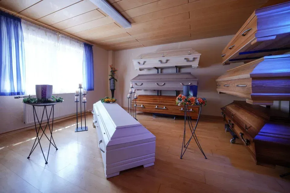 Ein Raum mit verschiedenen Särgen und Trauergestecken mit Kerzen
