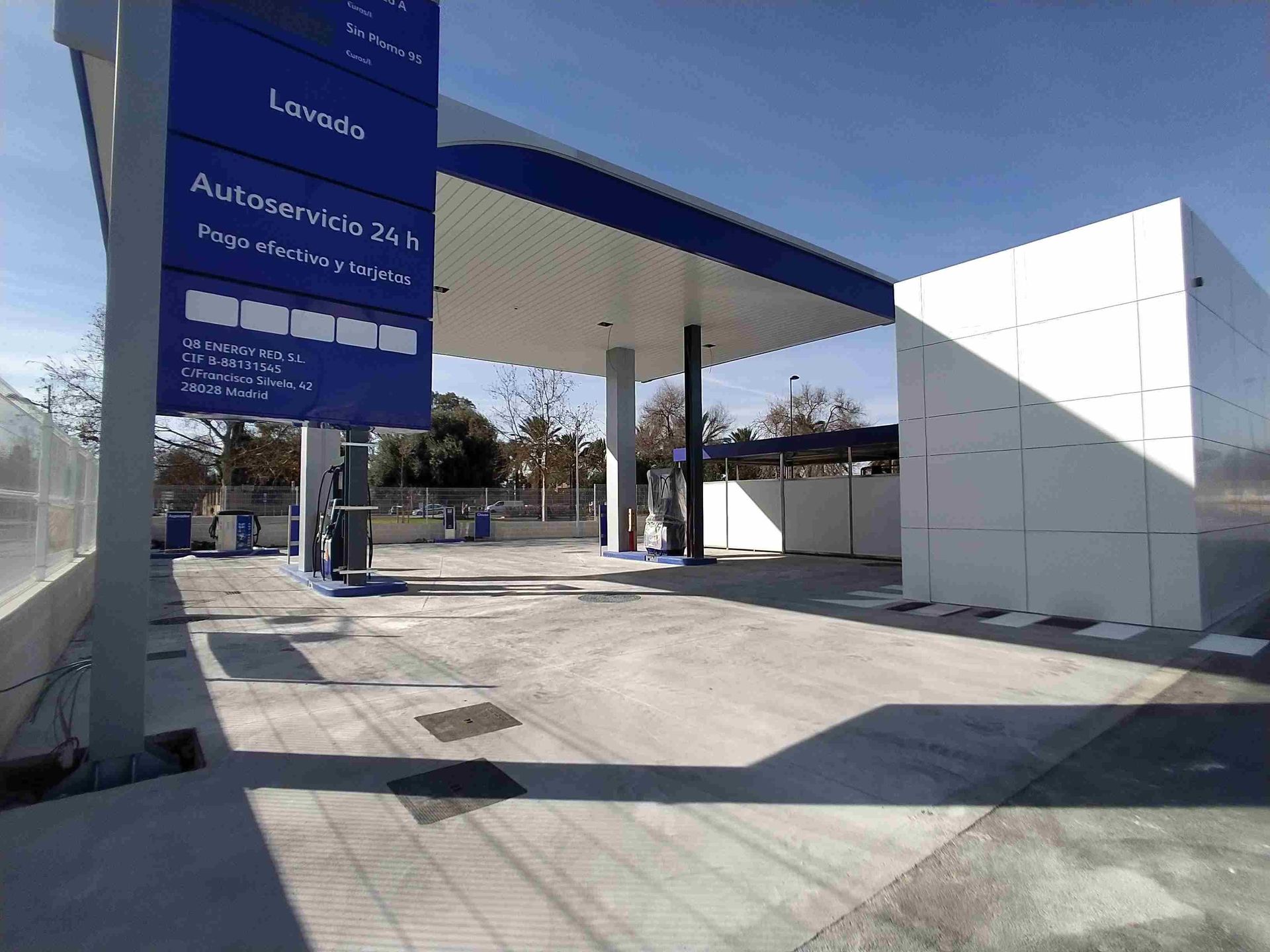 Una gasolinera con techo azul y un edificio blanco.