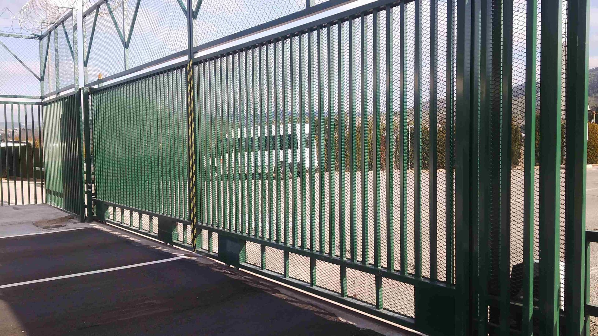 Una valla metálica verde rodea un estacionamiento.