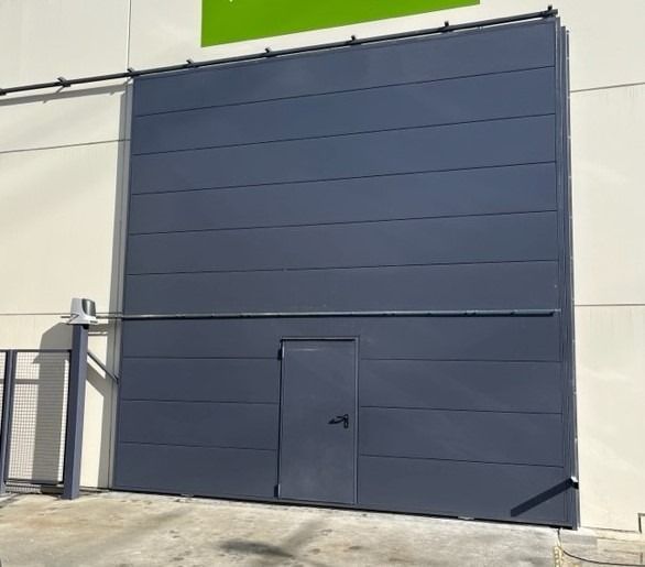 Una gran puerta de garaje negra con un cartel verde encima.