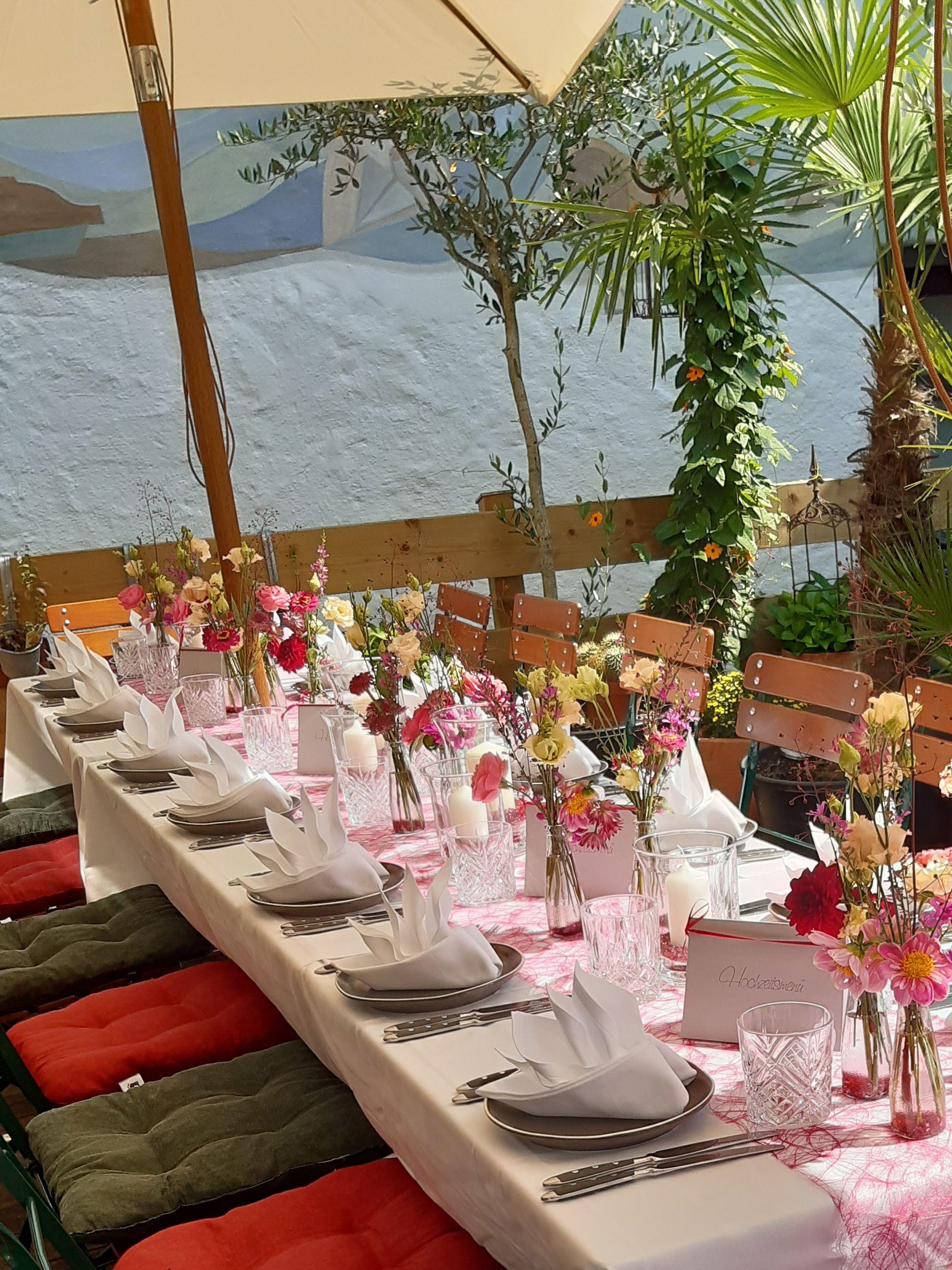 ein langer Tisch mit Tellern , Gläsern und Blumen darauf .