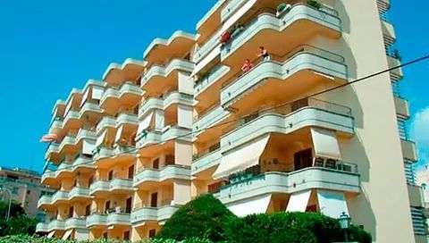 Un gran edificio de apartamentos con muchos balcones y un cielo azul al fondo.