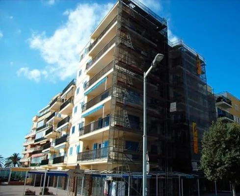 Un edificio alto con andamios a su alrededor y una farola delante.