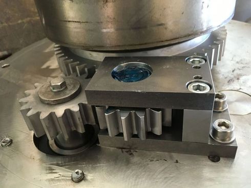 Nahaufnahme von Metallzahnrädern und einem bearbeiteten Bauteil auf einer Werkbank mit einem blauen runden Einsatz.