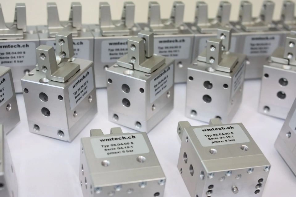 Reihen von silbernen Metallblöcken mit Löchern und Beschriftungen, angeordnet auf einer weissen Fläche.
