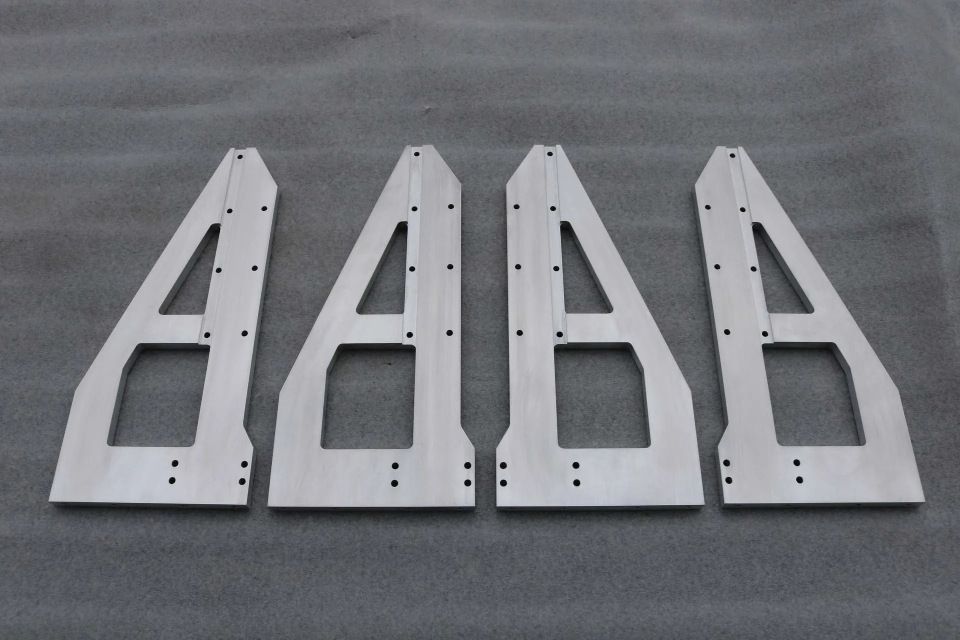 Vier silberne Metallhalterungsteile liegen nebeneinander auf einer grauen Oberfläche.