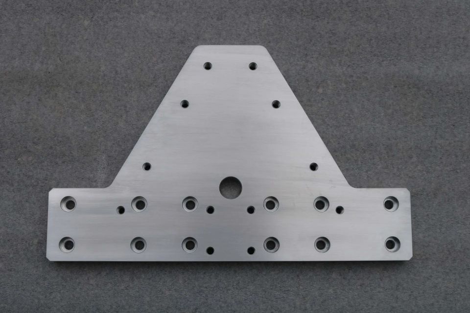 Graue Metallhalterung mit mehreren Bohrlöchern auf grauem Hintergrund