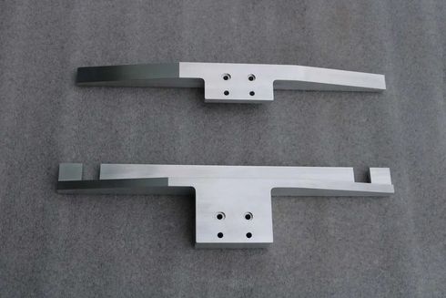 Zwei Schubladengriffe aus Metall, einer dunkel und einer silber, nebeneinander auf einer grauen Oberfläche.