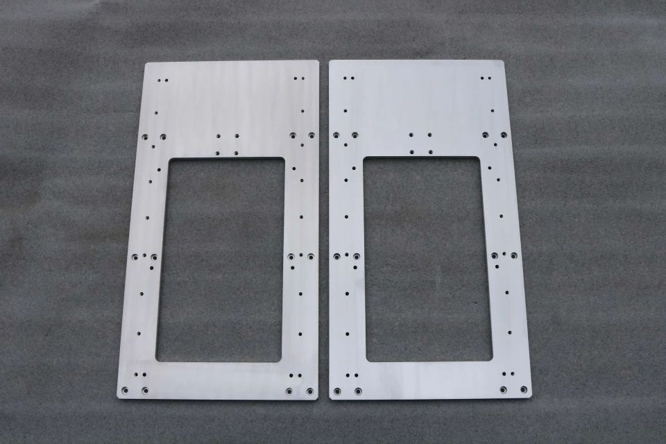 Zwei silberne Metallplatten mit rechteckigen Ausschnitten und verstreuten schwarzen Löchern auf grauer Oberfläche