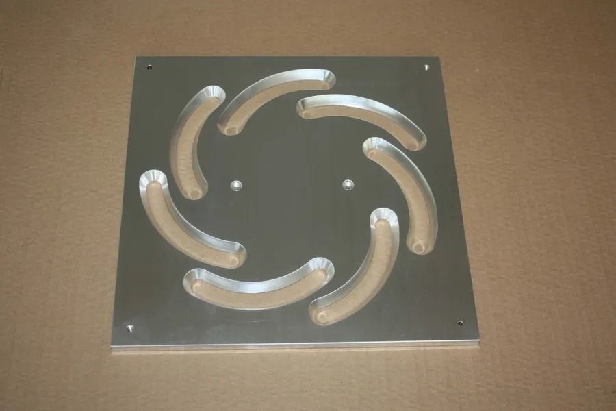 Quadratische Metallplatte mit sechs gebogenen silbernen Lamellen, die spiralförmig auf beigem Hintergrund angeordnet sind