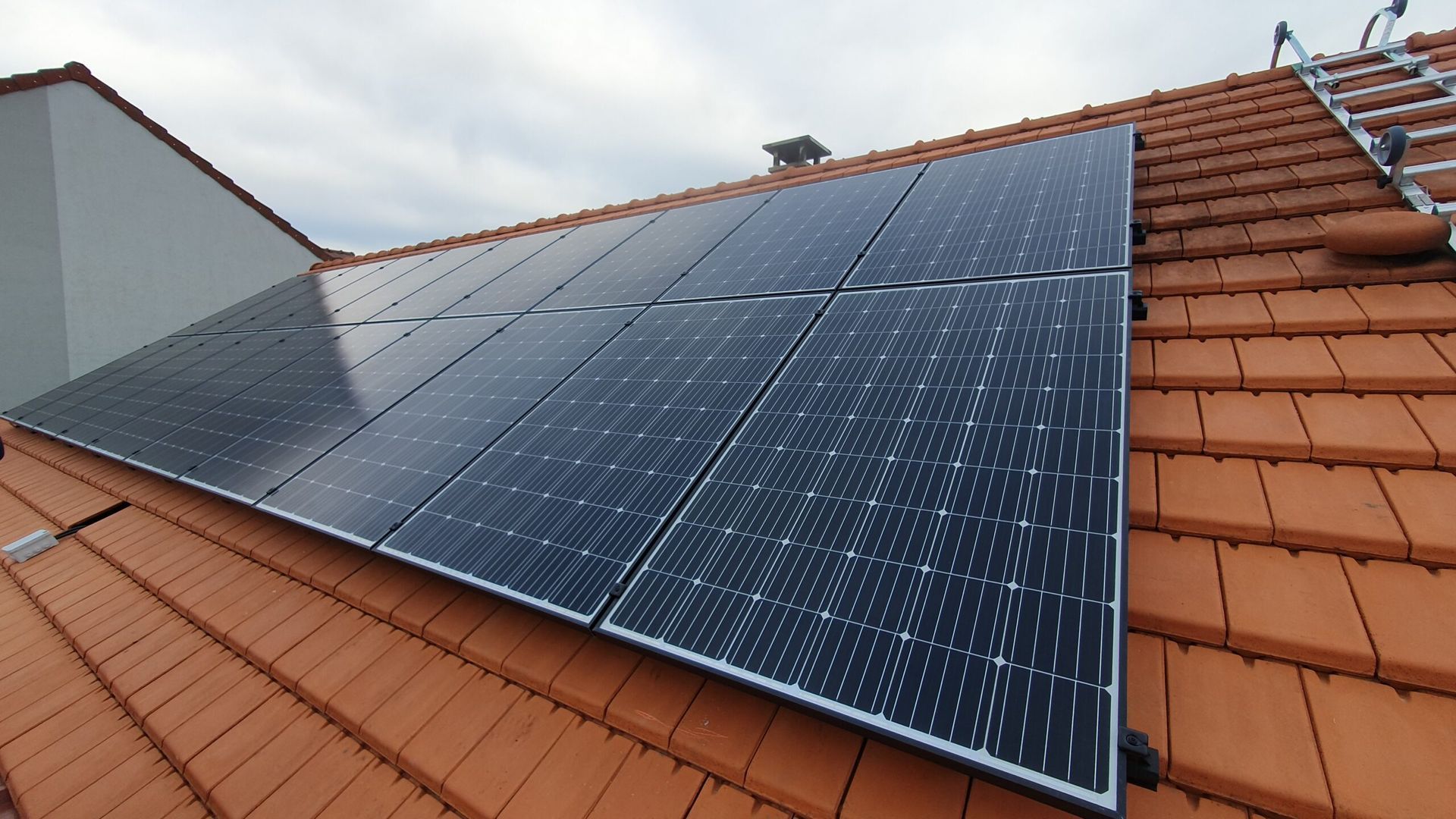 Panneaux solaires installés sur un toit de tuiles rouges, avec une échelle visible en arrière-plan.