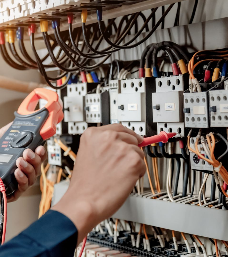 Un électricien utilise un multimètre pour inspecter les fils d'un panneau de commande.