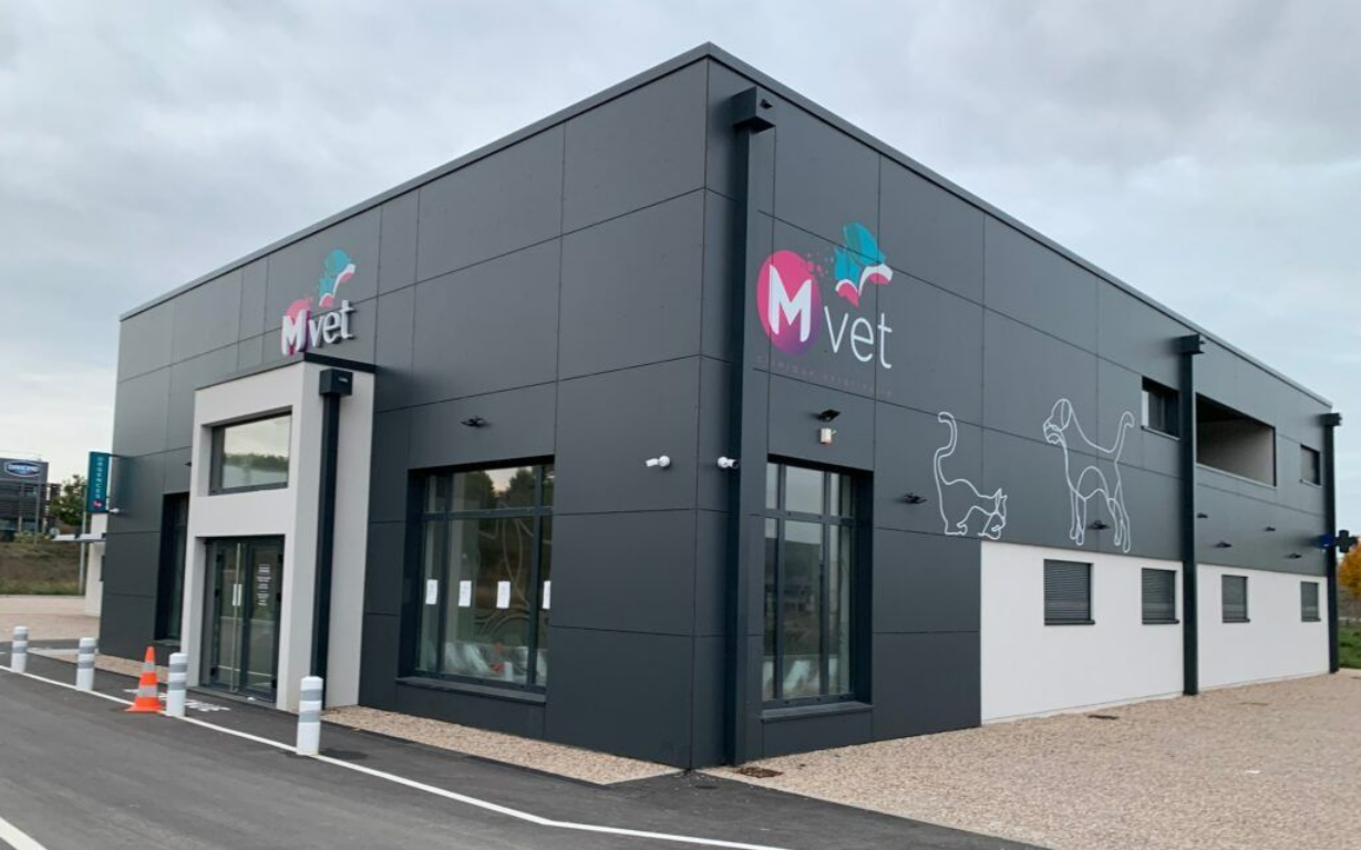 Extérieur d'une clinique vétérinaire moderne. Bâtiment gris avec logo rose M vet.