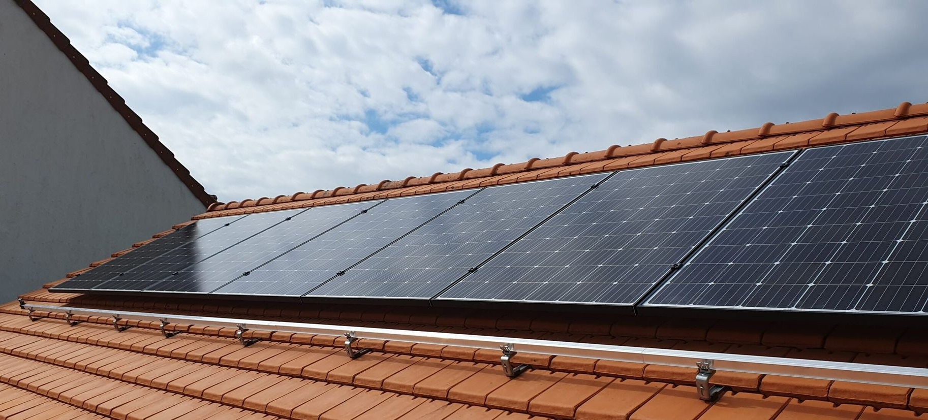 Panneaux solaires sur un toit de tuiles en terre cuite, se détachant sur un ciel nuageux.
