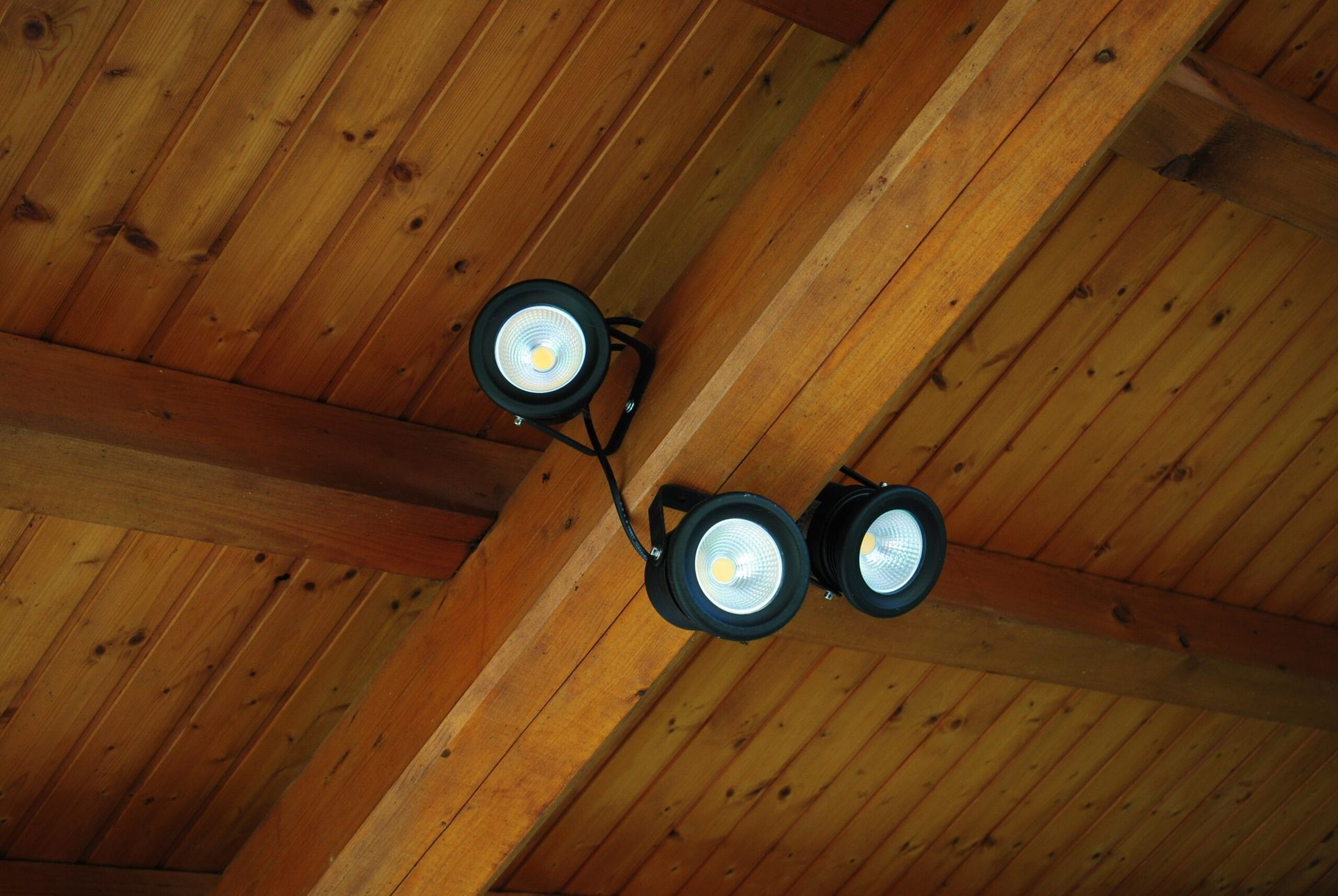 Trois spots LED noirs fixés à un plafond en bois.