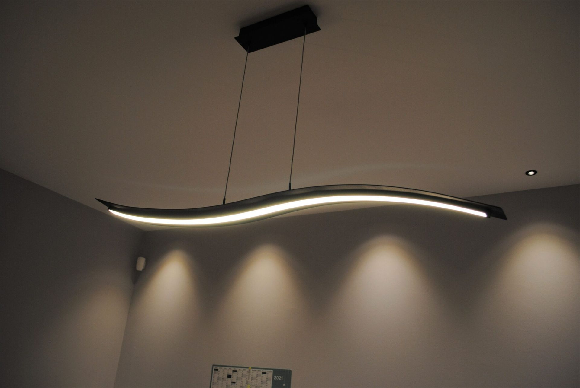 Une suspension lumineuse LED moderne et ondulée illumine une pièce en diffusant une lumière vers le bas.