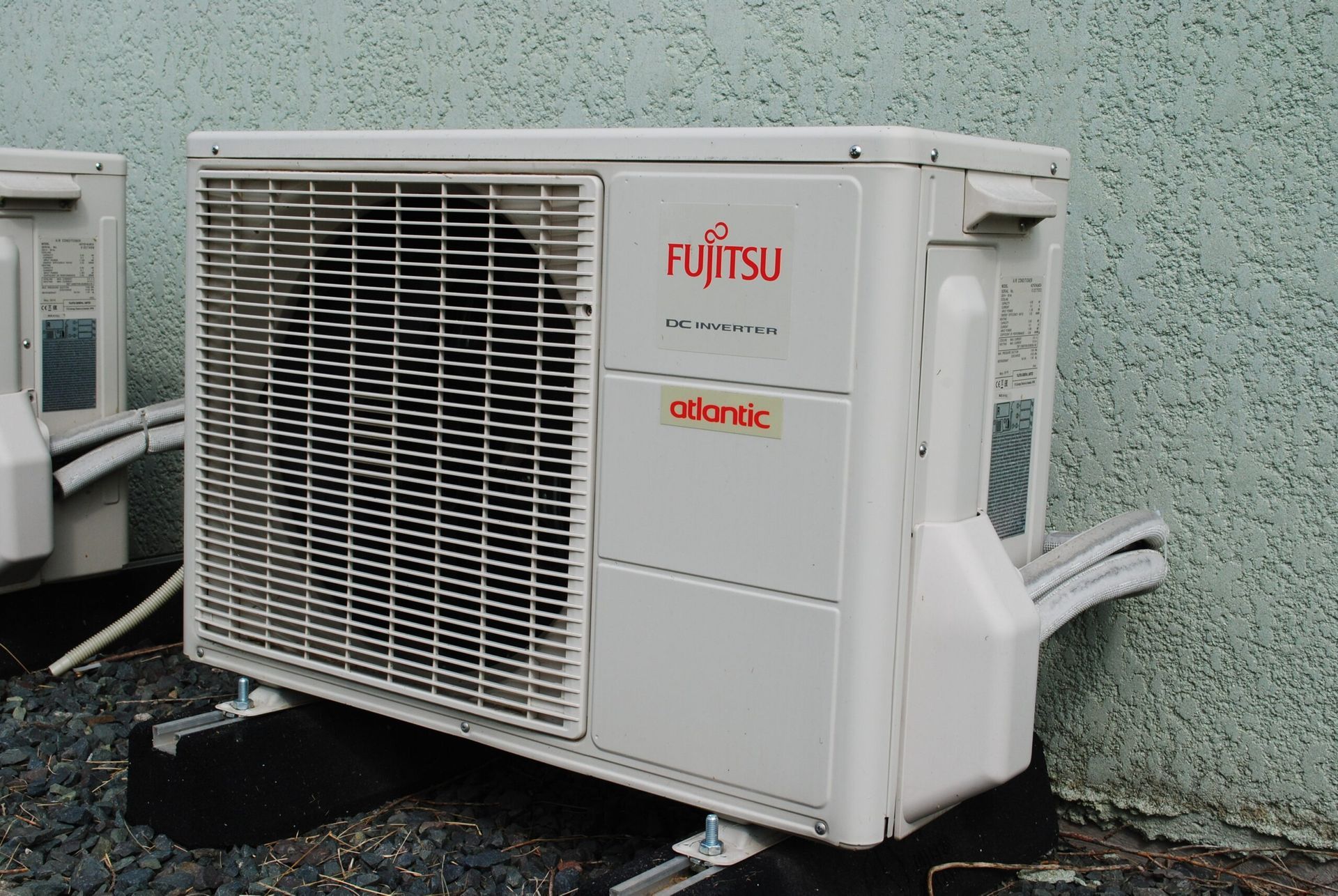 Unité de climatisation Fujitsu, blanche et beige, montée sur un socle noir, contre un mur gris.
