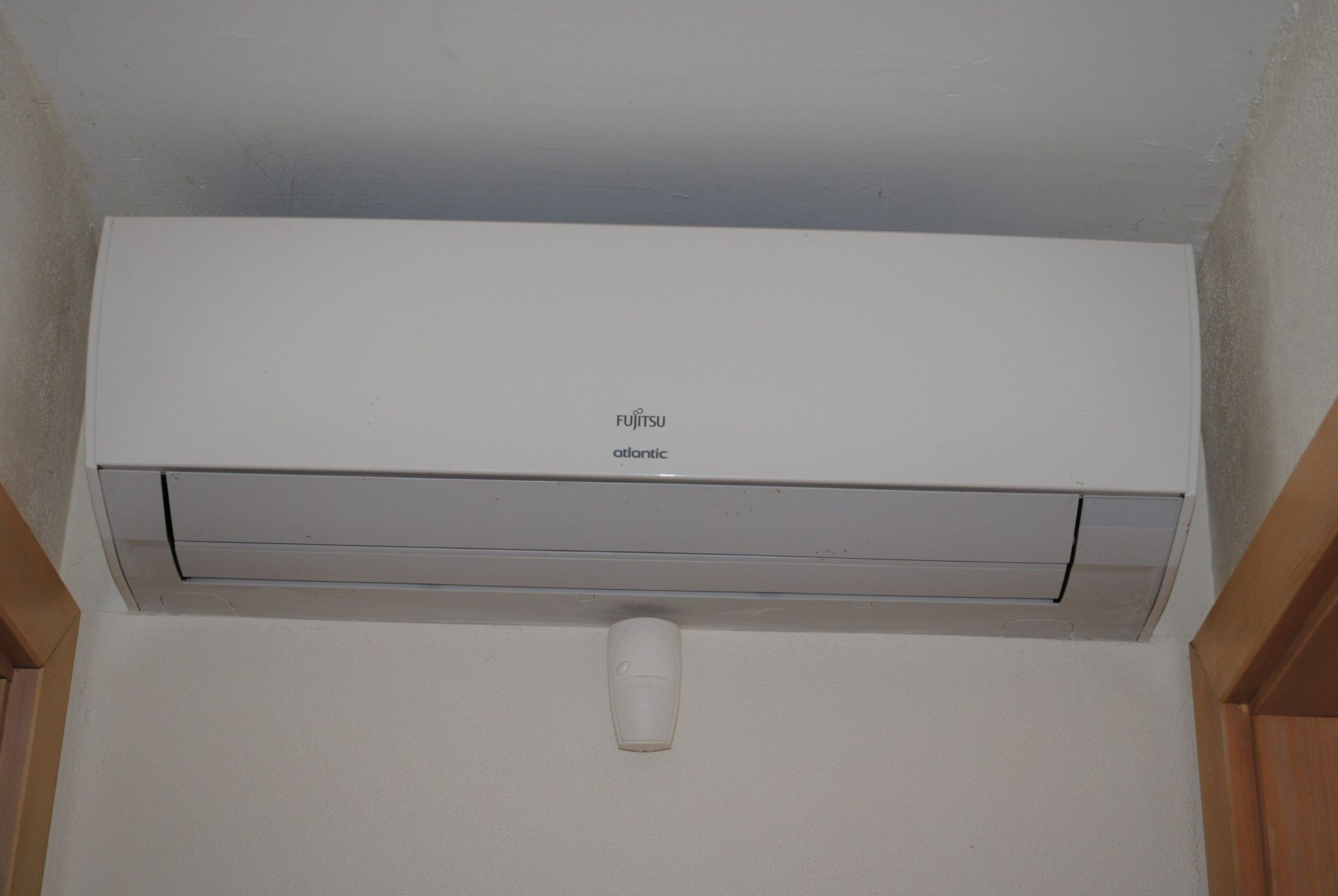 Climatiseur blanc fixé sur un mur blanc, au-dessus d'un petit tuyau d'évacuation.