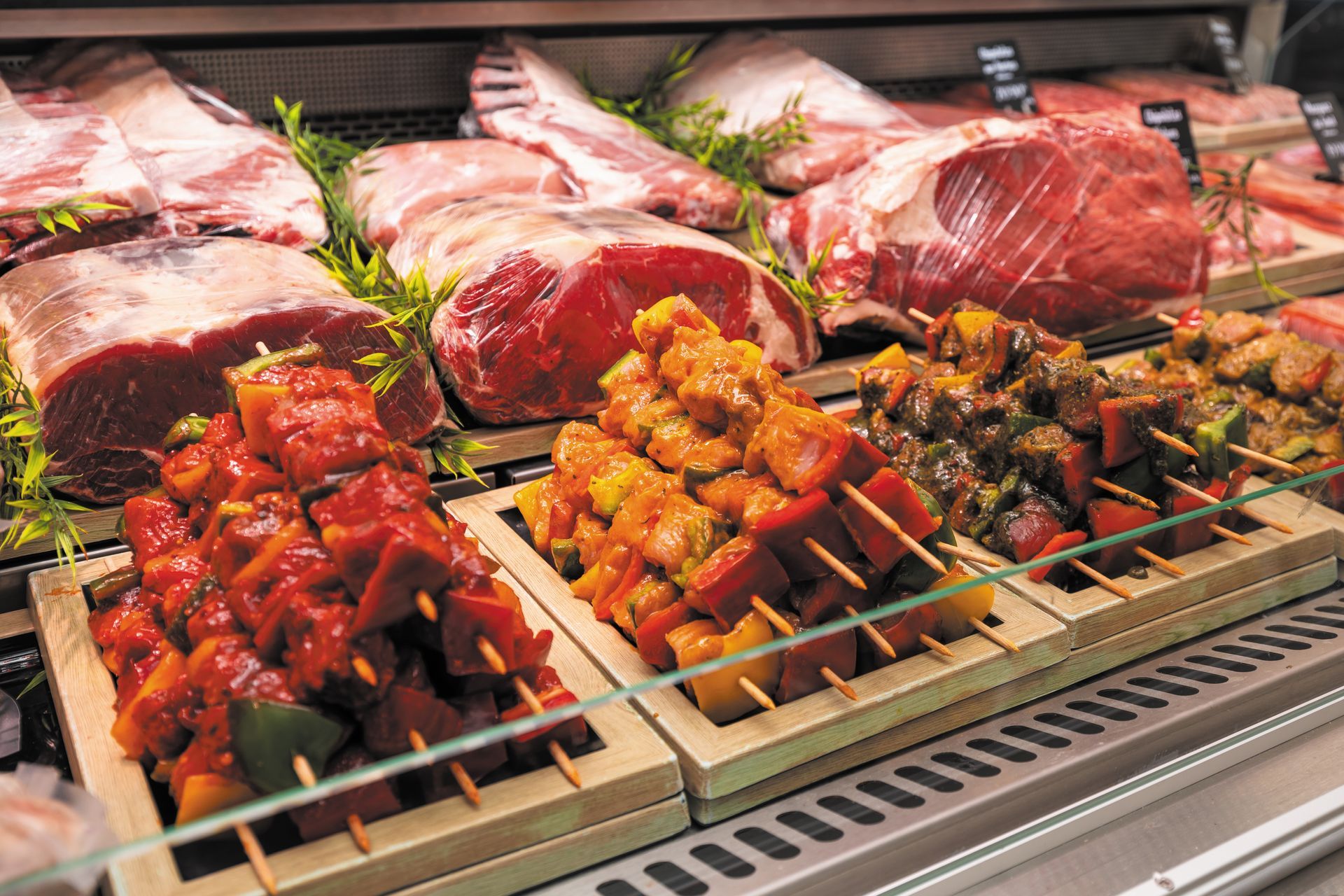 Vitrine de viandes crues assorties et de brochettes dans une boucherie, avec des morceaux rouges et marinés sur des plateaux.