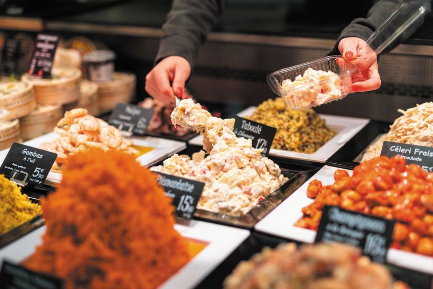 Des mains servent des salades et des amuse-gueules colorés variés au comptoir d'une charcuterie.