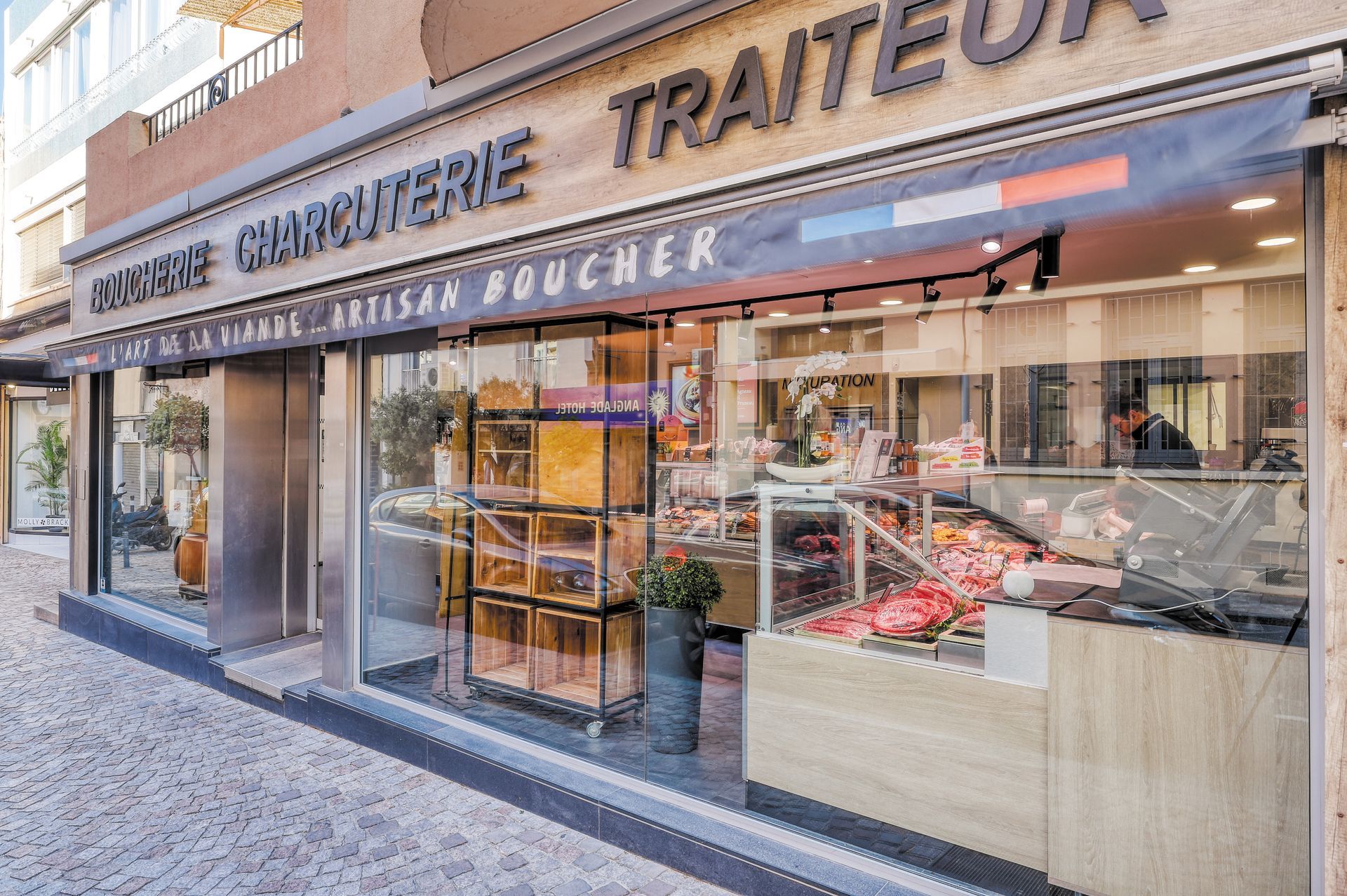 Boulangerie-charcuterie française avec vitrines et auvent, située dans une rue ensoleillée.