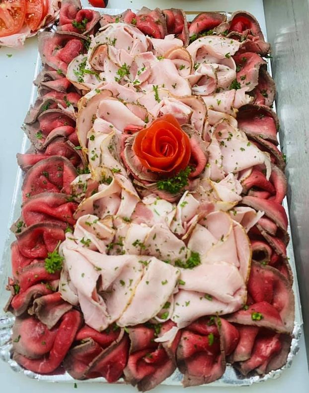 Plateau de charcuterie tranchée disposée en motif floral avec une rose de tomate en son centre.