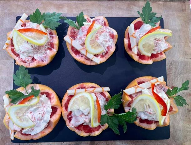 Six petites bouchées garnies de citron, d'herbes et de poivron rouge, présentées sur une planche d'ardoise noire.